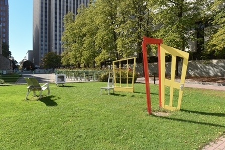 Bright colored metal doorway and window statues in a grass field.  Between them are metal chairs.