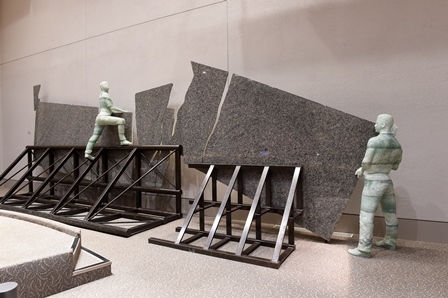 A statue made of granite, glass, and steel depicting two figures working together to lift building material.